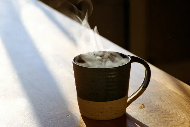 Tasse de café fumante posée au soleil sur une table en bois